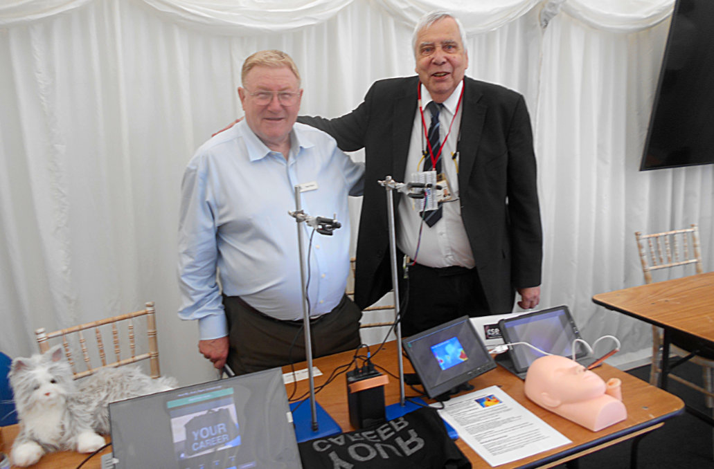 Roger and Ed smiling and standing at the CSES table with various interactive exhibits laid out