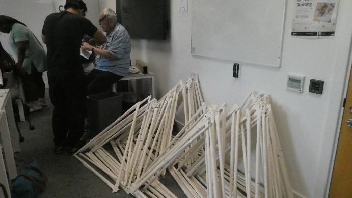 A pile of large triangles made of rolled paper tubes, stacked vertically against the wall